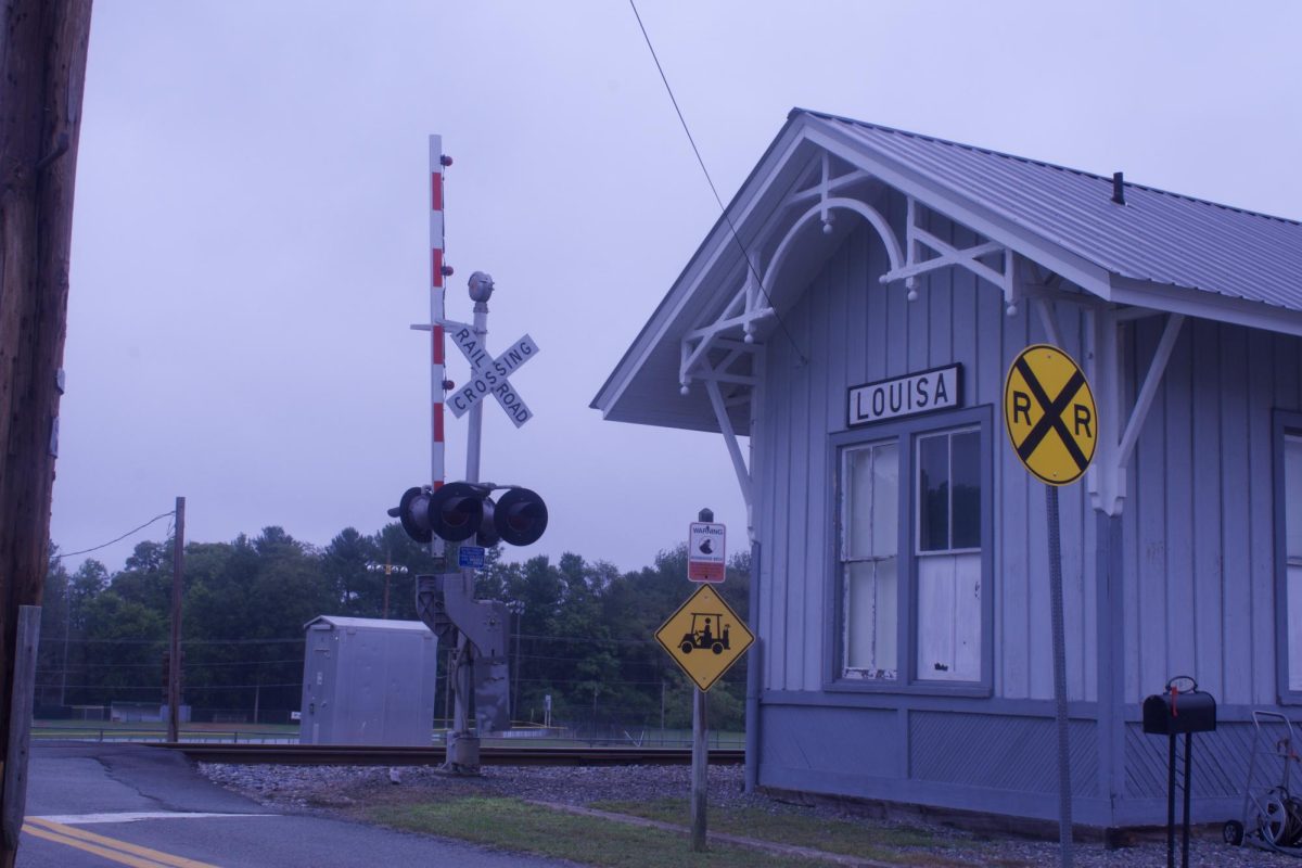 The railroad sign and light warning and showing the train tracks and the train depot.