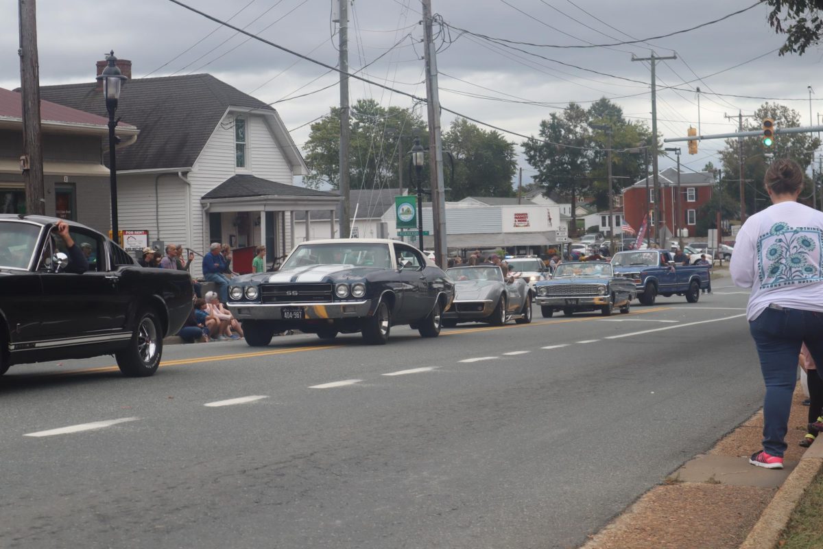 A group of cars throw candy to children on center street and parade their county pride. 