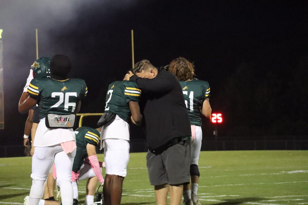 Coach Jeff Alston praying separately with wide receiver Isaiah Haywood before the game while players get ready 