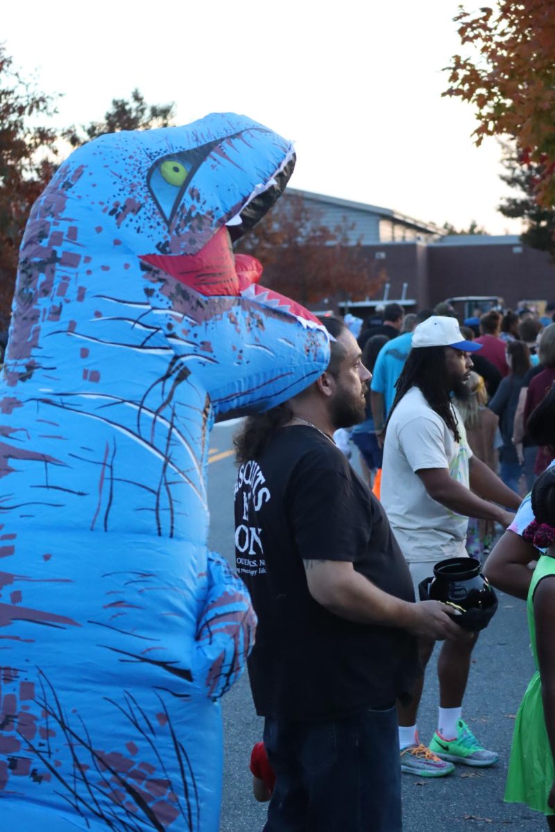 Blue inflatable dinosaur costumed trick or treater waits in line with the Louisa community for candy. 