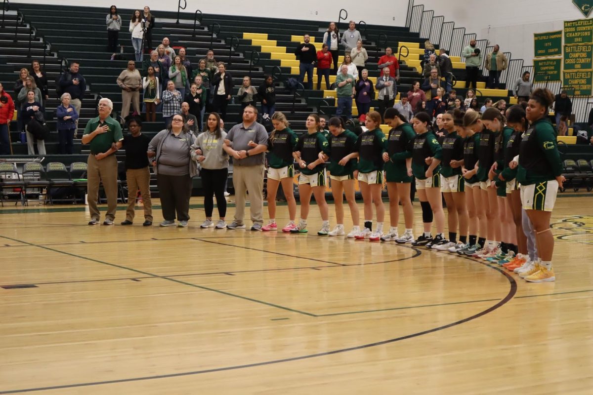 Lady Lions varsity basketball team stands along the three point line during the National Anthem 