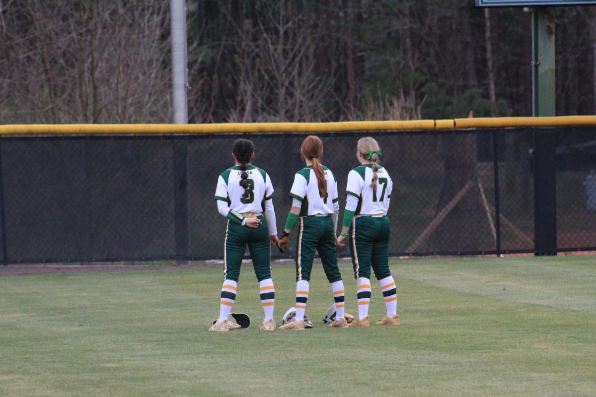 three softball outfielders standing together during the national anthem.