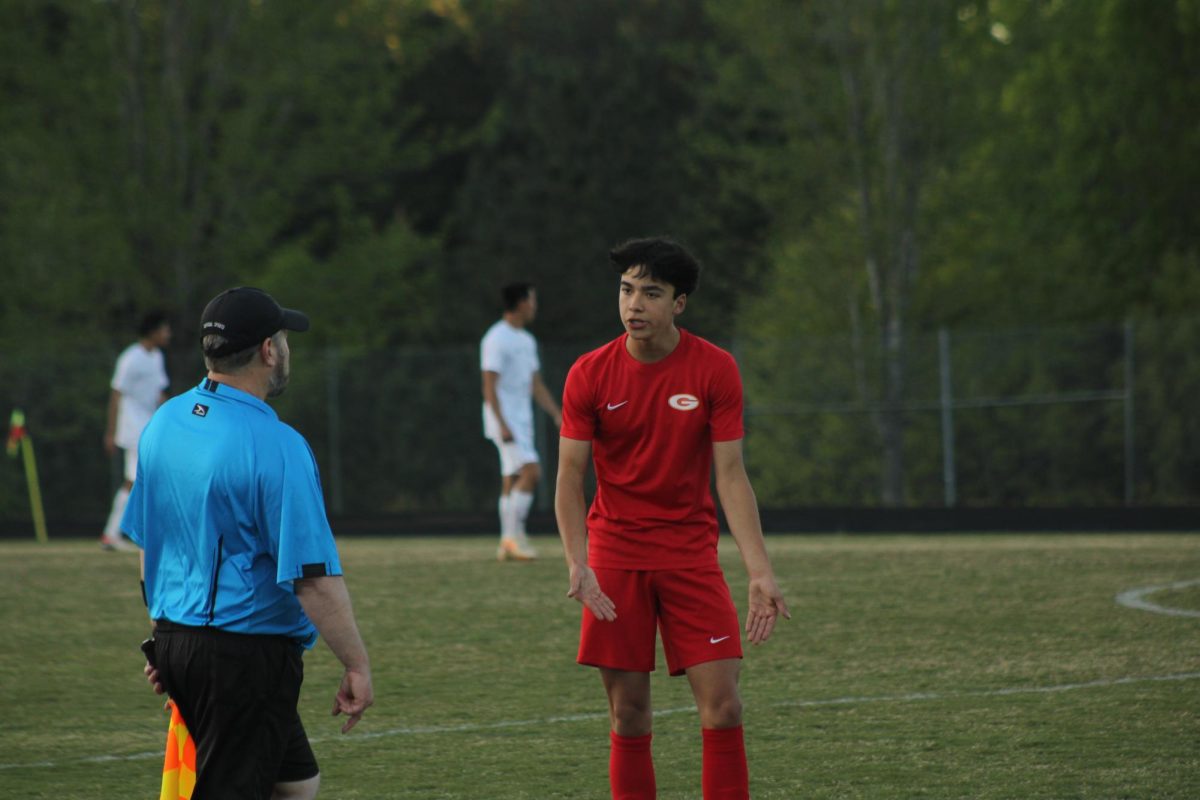 Goochland player arguing with the referee about a call to Louisa players, #20 Peyton Pekary and #9 Larson Moreno, needing to change their gear. 