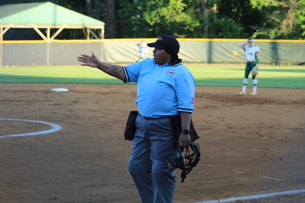 An umpire at a high school softball game directing the players to the correct spot. 