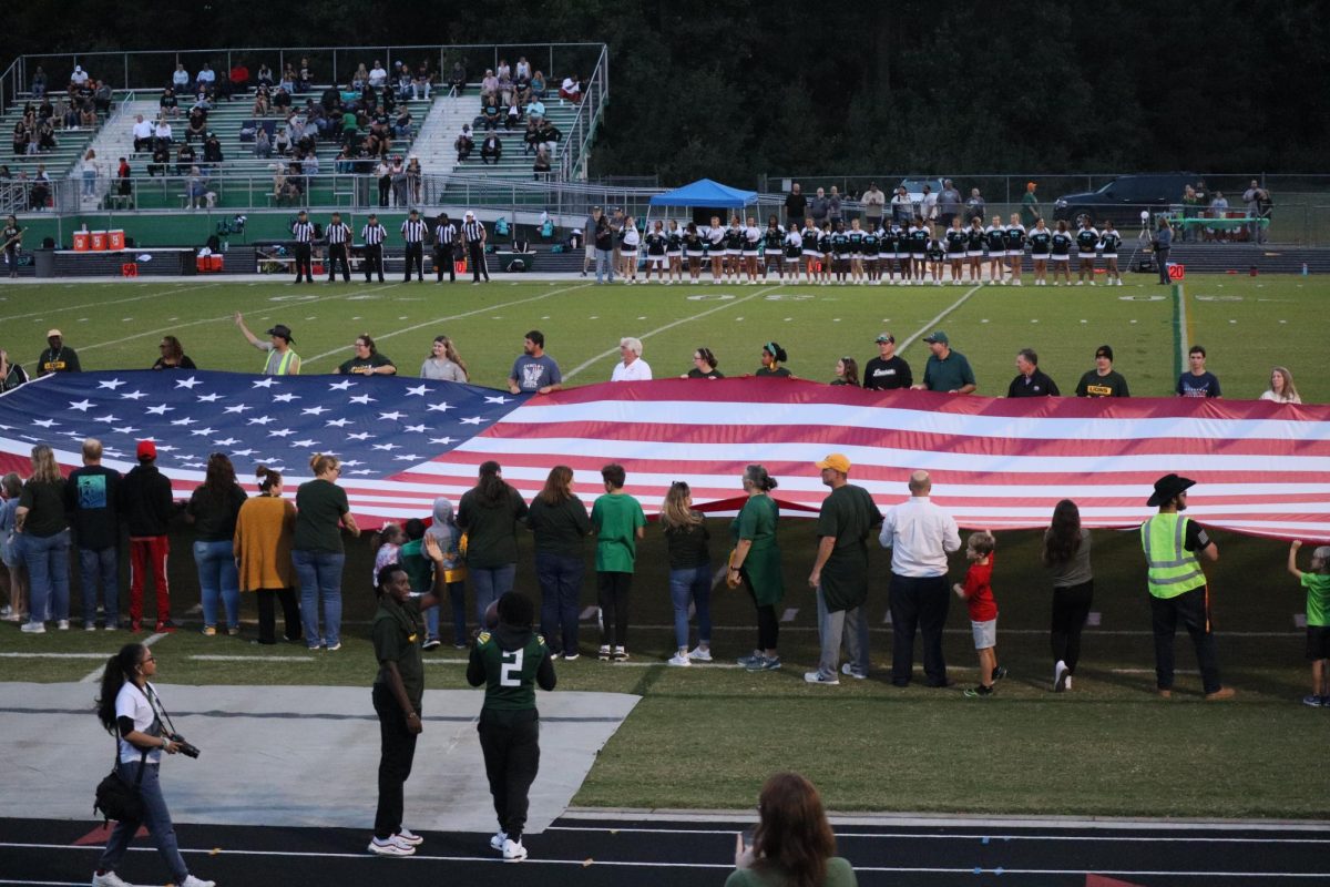 Louisa patrons gather to hold the American flag to say the Pledge of Allegiance before kickoff.