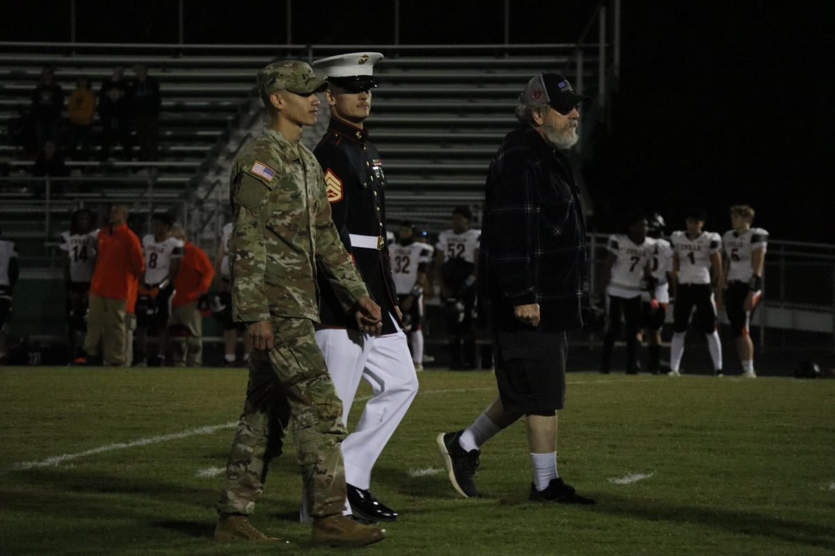 Two active duty soldiers walk the field next to a veteran on military recognition night. 