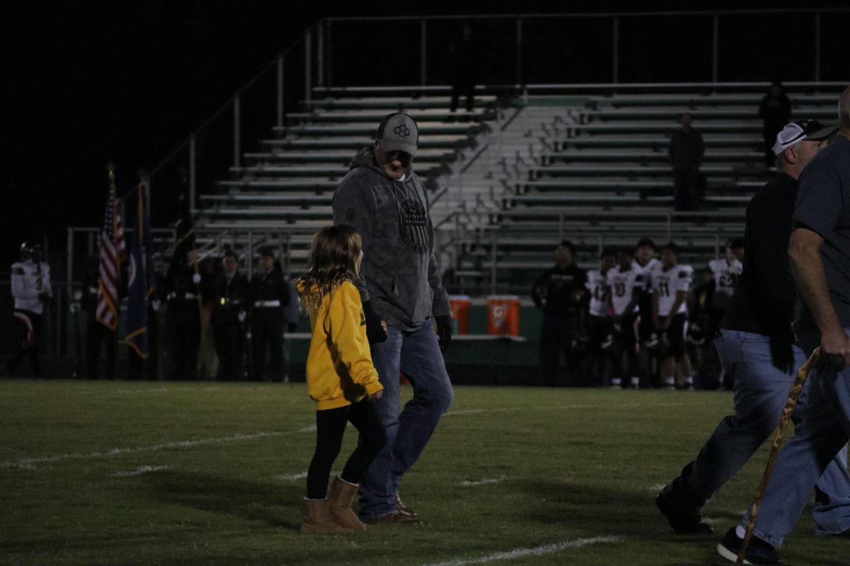 A dad smiles at his daughter as they both walk the field for military appreciation night. 