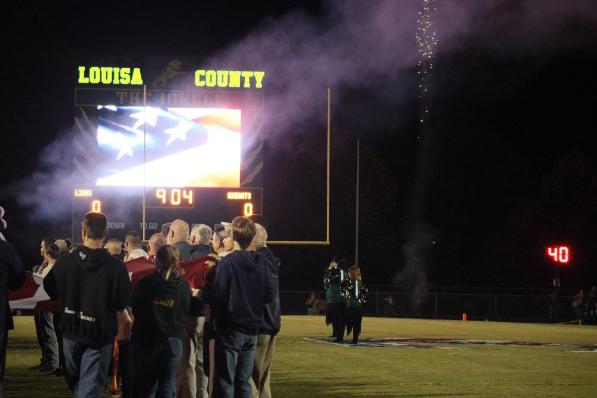 Students, adults, and community members take part in holding the flag during the National Anthem.