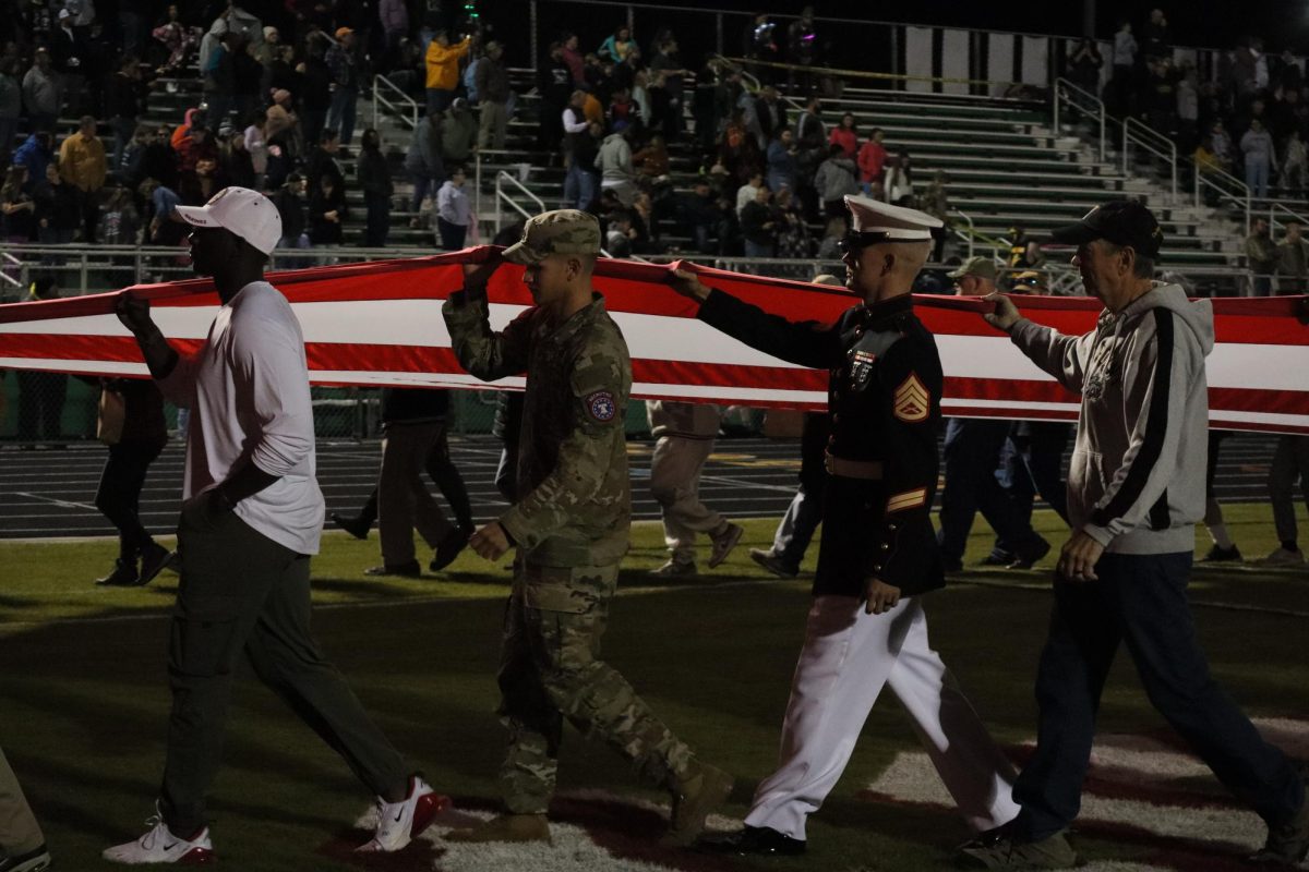 Community members and military soldiers take part in walking the flag off the field.