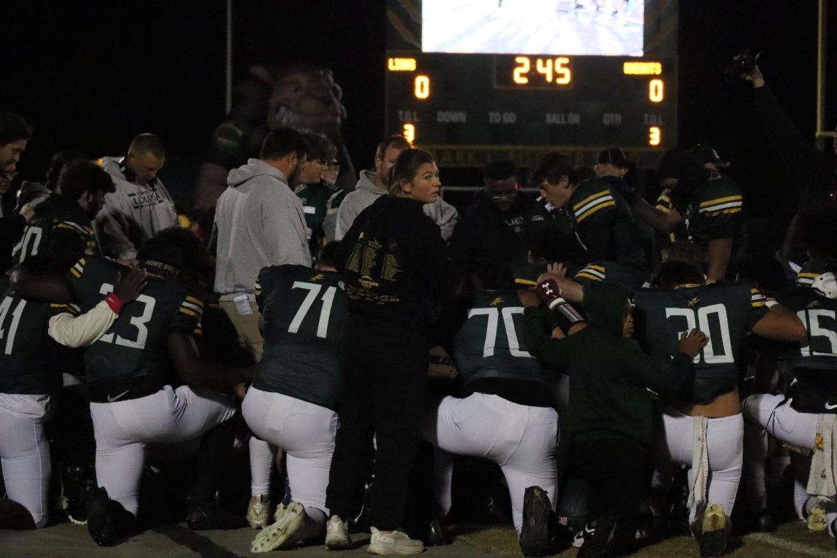 The football team huddles together as senior Luke Rowan says a prayer before the game. 