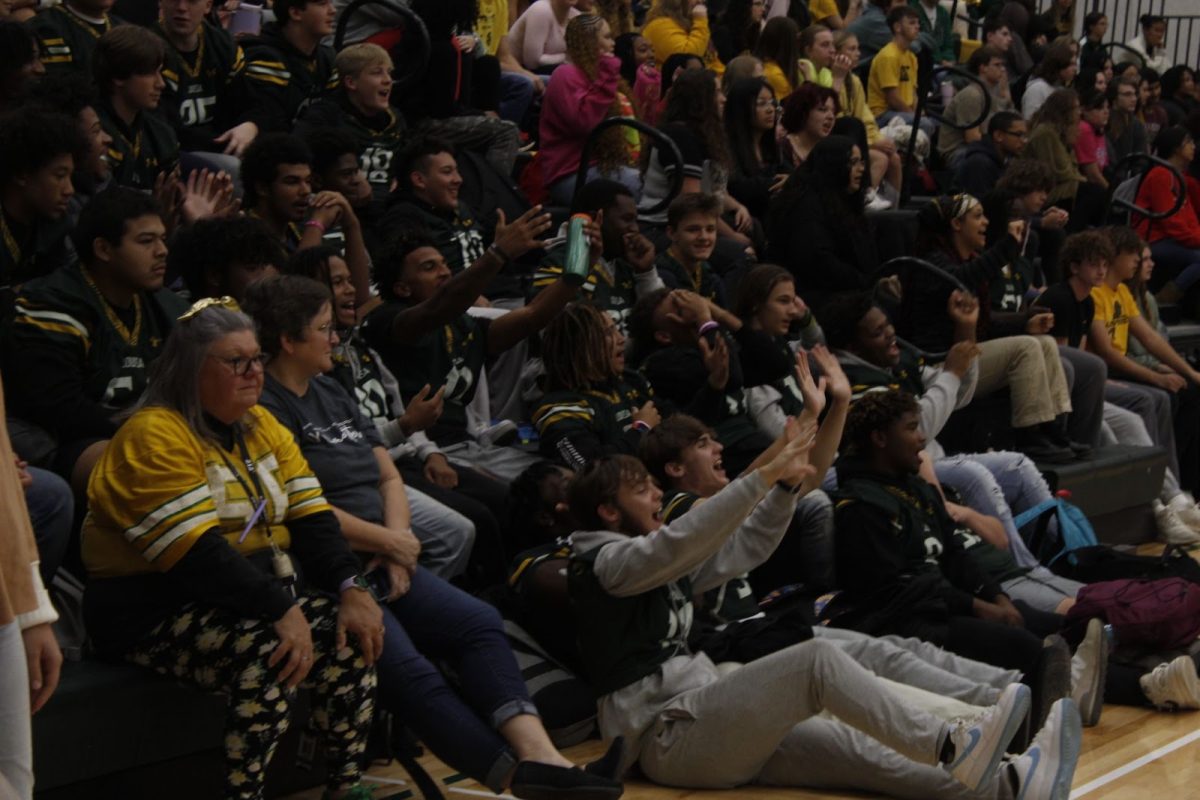 Varsity football players lift their hands into the air while singing along to a song.