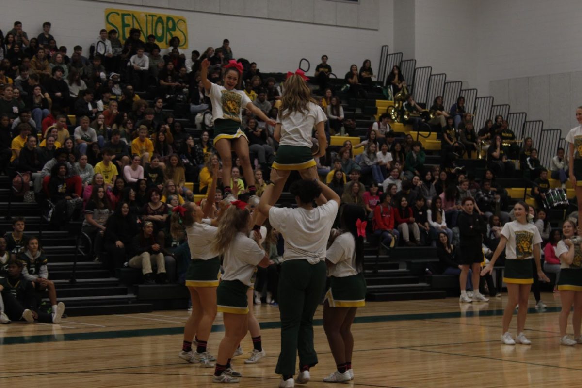 Competition Cheerleaders reenact running a play in football with the fliers in the air. Junior Sophia Braxton (flyer) falls back after being “tackled.”
