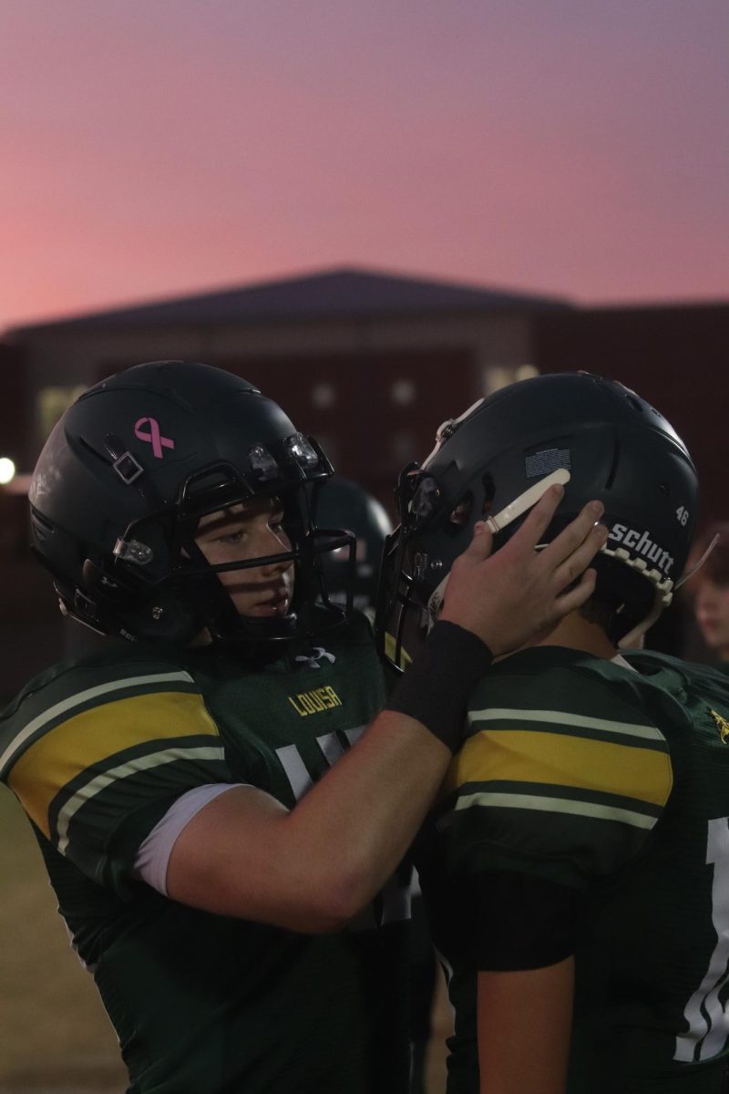 Players helping Player fix his chinstrap on his helmet before kick-off