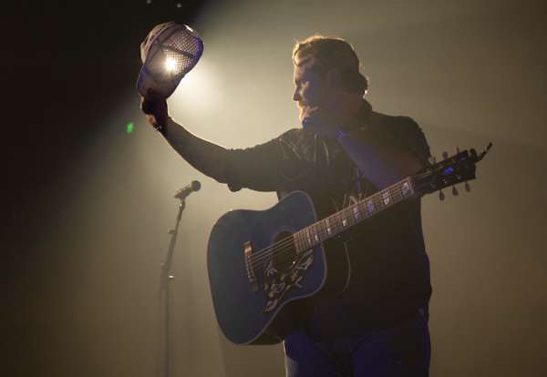 ERNEST holds his hat as he looks out into the audience at the Ryman Auditorium in Nashville, Tennessee. Image courtesy of Corey Miller, ernestofficial.com.