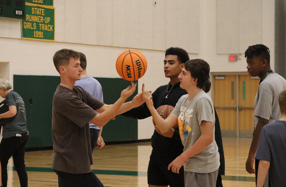 Basketball player Patrick Moore helping teach students to spin a basketball on their finger during basketball clinic.