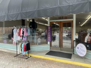 Clothes hang outside of the store along with a welcome sign, welcoming customers in.