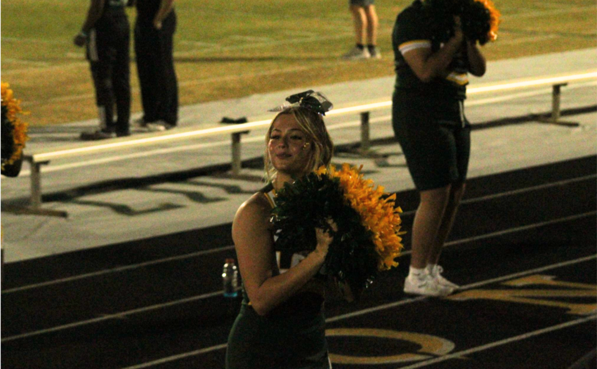 Cheer captain, Peyton Brady, shakes her pom-poms to inspire a spirited feeling  amongst the fans. 
